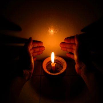 Hands cupping around a burning candle